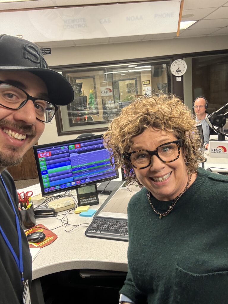 Robbie Daniels, host of the Morning Show on KFGO, posing in the studio with Jeff Carney, owner of DarkHorse IT, in front of microphones and monitors.